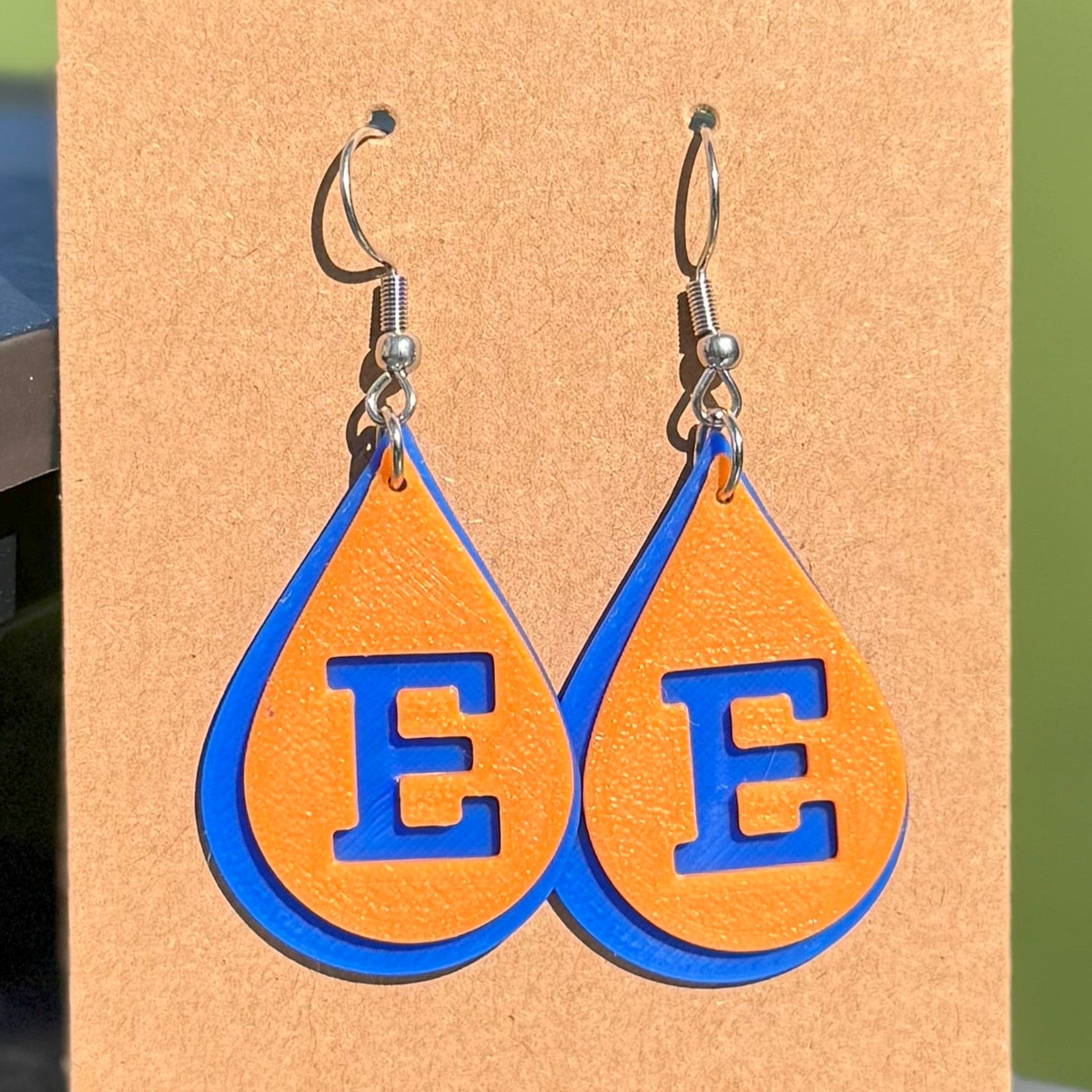 Teardrop-shaped earrings with 'E' letters on a cardboard backing